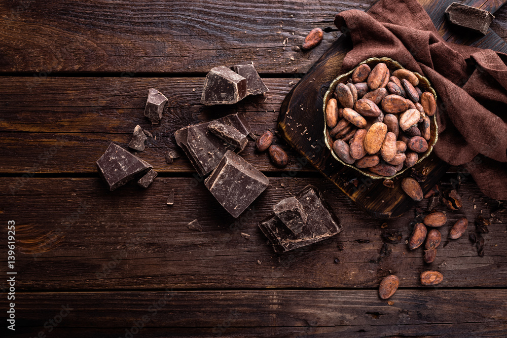 Cocoa beans and chocolate on wooden background - obrazy, fototapety, plakaty 