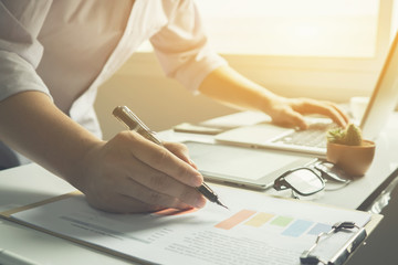 Business man working at office with laptop and documents on his desk, consultant lawyer concept,young male student typing and writing on business chart sitting at wooden table,vintage color