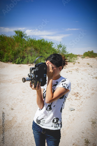 Fotografie, Obraz Girl Shooting 16mm Film Camera in Desert