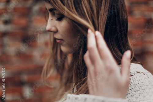 Fotomural stylish hipster gypsy woman posing in knitted sweater on background of brick wall, holding hair