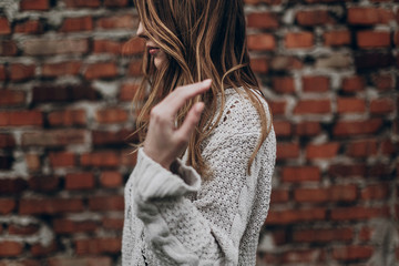 Wall Mural - stylish hipster gypsy woman posing in knitted sweater on background of brick wall, holding hair. atmospheric sensual moment. boho country fashionable look. free people