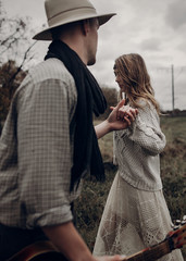 Wall Mural - stylish hipster couple holding sensually hands. boho gypsy woman and man in hat embracing in windy field. atmospheric amazing moment. fashionable look. rustic wedding concept