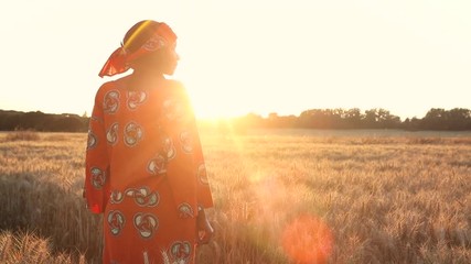 african woman in traditional clothes standing in a field of crops at sunset or sunrise