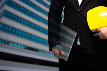 Wall Mural - double exposure of professional engineer hold in hand yellow safety helmet and laptop business and industrial concept on building business district city background, color tone effect, copy space.