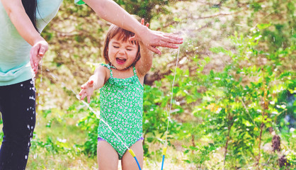 Wall Mural - Toddler girl playing in a sprinkler with her mother