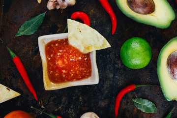 Hot mexican salsa whith the nacho chips surrounded by ingredients - tomatoes, chili peppers, lime.