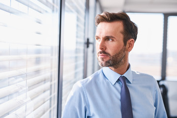 Canvas Print - Portrait of handsome businessman standing at office looking out the window