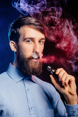 Young guy with a beard vaping and releases a cloud of vapor. hipster vaper smoke vaporizer.