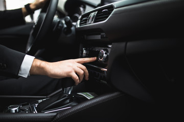 close up of young man in suit driving car and switching some button on panel of car