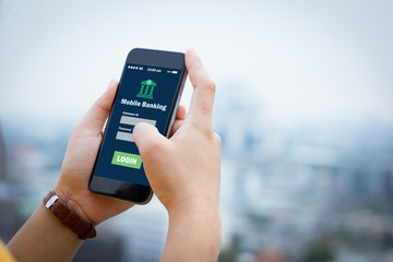 female hands hold mobile banking on smart phone on blurred urban city as background