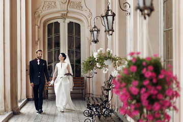 Wall Mural - elegant gorgeous bride and stylish groom walking holding hands, sensual touch on background of old building. unusual luxury wedding couple in retro style.