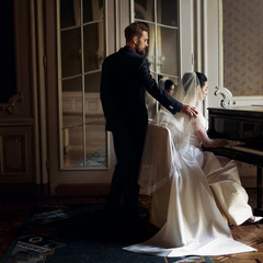 Wall Mural - elegant stylish handsome groom hugging gently gorgeous bride while playing the fortepiano. unusual luxury wedding couple in retro style