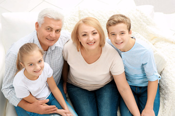 Wall Mural - Cute children with grandparents sitting on sofa in living room