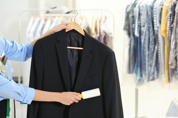 Woman with adhesive roller cleaning clothes in dry-cleaning salon