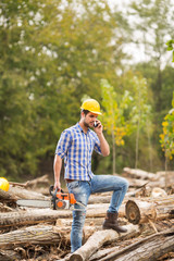 Wall Mural - Guy, with yellow helmet on his head, talks on the phone and holds a chainsaw in his hand