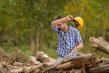 Wall Mural - Tired young woodcutter wipes the sweat from his forehead