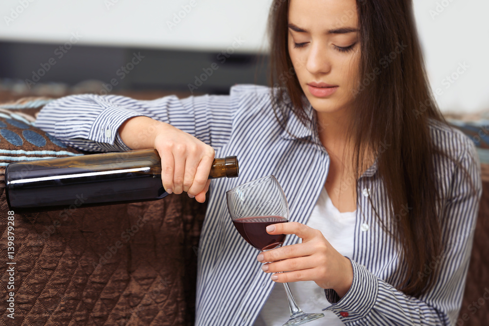 Depressed woman drinking wine indoors