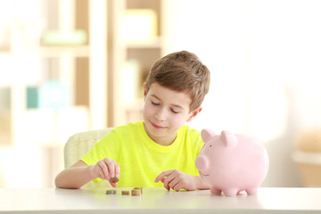 Canvas Print - Little boy saving coins in piggy bank at home