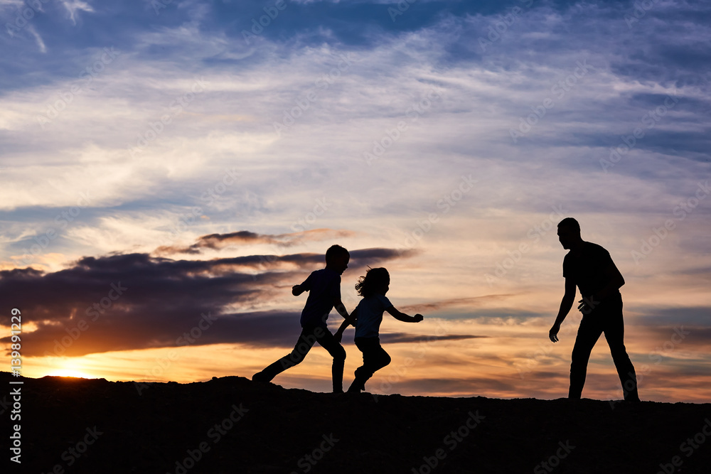 Father and children on the beach at the sunset time. Concept of friendly family. - obrazy, fototapety, plakaty 