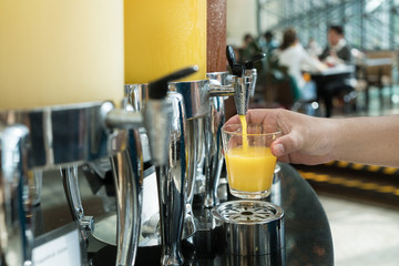 Wall Mural - Hand holding glass refill orange juice for row of fresh juice at buffet restaurant, Juice buffet self service in morning at hotel.