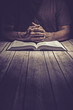 Man praying on a wooden table with an open Bible