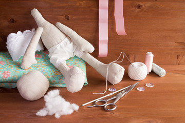 Textile doll in the sewing process with accessories and materials: lace, fabric, thread, needle, scissors. On wooden background