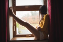 Woman Sitting At Window Sill And Looking Outside