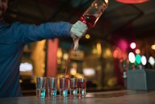 Bartender Pouring Alcoholic Drink In Shot Glasses