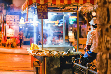 Male street fast food seller with pan corn on traditional turkish cart. Istanbul, Turkey. Night scene.