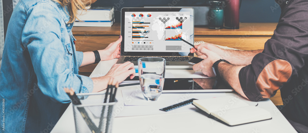 Businessman and businesswoman sitting at table in front of laptop and working. Graphs,charts and diagrams on PC screen. - obrazy, fototapety, plakaty 