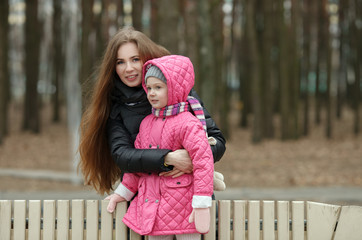 Happy young mother and child daughter hugging posing on bench in spring park