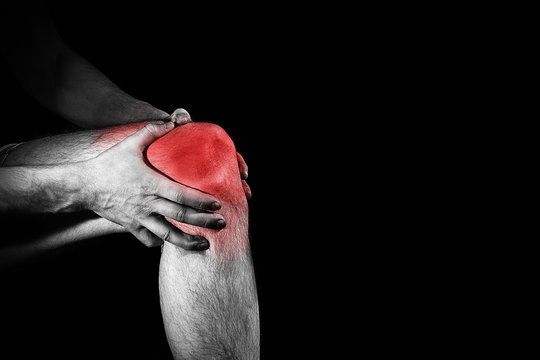 Fototapete - man, holding her painful  Knee,  leg, experiencing pain,  red spot, on the black background, Sport injury