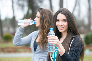 two young woman drinking water in a park