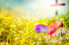 Easter Background With Colorful Painted Easter Eggs In The Grass, With Spring Flowers And A Cross In The Background. Easter Resurrection Religious Background With Copy Space For Text.