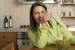 © Gudrun - Young woman with brown hair is sitting in front of a glassy bowl with peas in the kitchen and is laughing, close-up