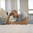 © STOCK4B  - Young man in a Pajamas laying in bed next to a laptop