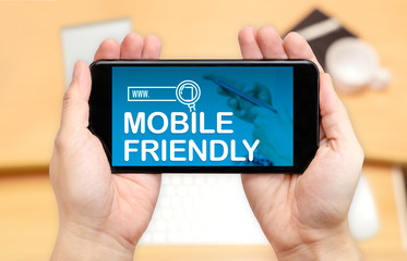 Wall Mural - watching two hand holding mobile phone with mobile friendly word on screen and blur desk office back