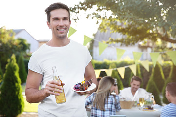 Sticker - Young man holding bottle of beer and plate with grilled meat and vegetables