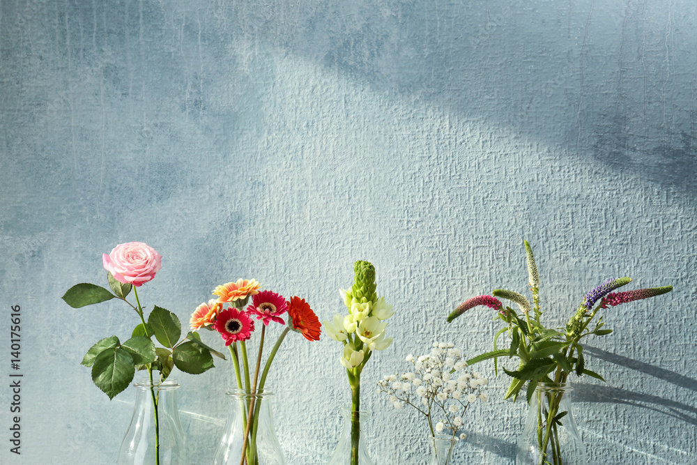 Beautiful flowers in glass vases on textured wall background