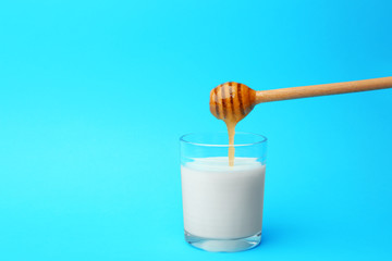 Canvas Print - Pouring honey into glass of milk on blue background