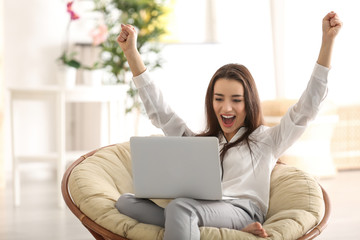 Young woman with laptop sitting on armchair at home