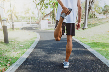 Young man stretching bodies, warming up for jogging in public park.