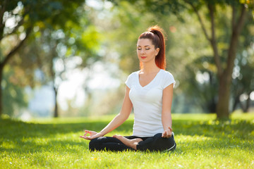 Wall Mural - Yoga outdoor. Happy woman doing yoga exercises, meditate in the park. Yoga meditation in nature. Concept of healthy lifestyle and relaxation. Pretty woman practicing yoga on the grass