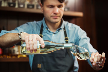 Wall Mural - Male sommelier pouring white wine into long-stemmed wineglasses.