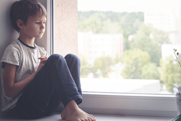 Sad child sitting on window shield and looking out the window