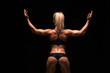 © satyrenko - Beautiful athletic woman in sporty cloths is posing, holding hands up and showing her perfect body, back view isolated on dark background with copyspace