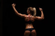 © satyrenko - Beautiful athletic woman in sporty cloths is posing, holding hands up and showing her perfect body, back view isolated on dark background with copyspace