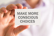 Businessman holding a card with MAKE MORE CONSCIOUS CHOICES message