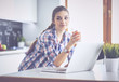 © lenets_tan - Young woman standing in kitchen using laptop