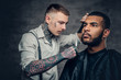 © Fxquadro - Tattooed barber makes haircut to a Black bearded male.